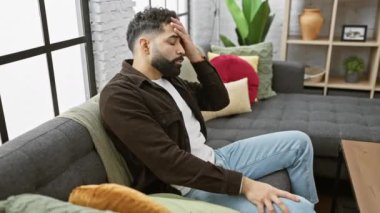 Çapraz kollu İspanyol genç adam evde yorgun ve sıkılmış görünüyor, depresyon sorunlarını düşünüyor..