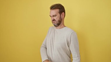 Yakışıklı, orta yaşlı, tiksinti içinde elleri havada bir İspanyol. Ürkütücü ifadesi, izole edilmiş sarı arka planda hoşnutsuz bir nefret tepkisi gösteriyor..