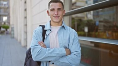 Şehir sokağında kollarını kavuşturmuş genç İspanyol bir adam kendine güveni ve günlük tarzını sergiliyor..