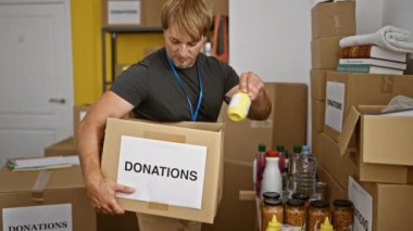 Depoda sakallı bir adam yiyecek bağışlarını karton kutulara dolduruyor.