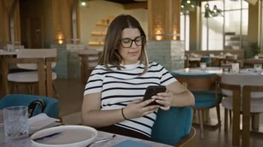 Esmer bir kadın modern bir restoran ortamında akıllı telefon kullanarak gündelik ve bağlantılı bir hayat sürüyor..