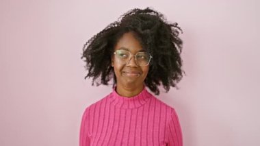 Kendinden emin, düşüncelere dalmış, gülümseyen yüzünü çeviren Afro-Amerikan kadın. Gözlük takıyor, pembe bir arka planda güzellik tasavvur ediyor.. 