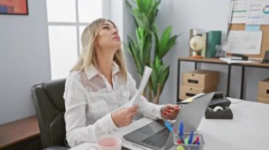 Bir kadın, modern ofis ortamında masasındaki belgeleri gözden geçirir. Bilgisayarı ve ofis malzemelerini görünür hale getirir..