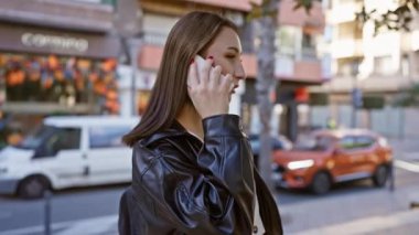 Genç esmer kadın, kalabalık bir şehir caddesinde yürürken telefonla konuşuyor..
