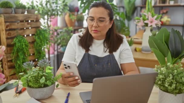 Зріла Іспаномовна Жінка Використовує Смартфон Ноутбук Квітковому Магазині Оточенні Зелених — стокове відео