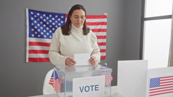 成熟したヒスパニック系女性がアメリカの選挙室で投票し 背景にはアメリカの国旗がある — ストック動画