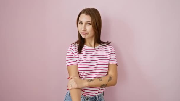ストライプTシャツのハッピー若いブルネットは ピンクの孤立した背景の上のカメラを見て 笑顔を信頼して側面を指す 歓迎ジェスチャー 製品広告に最適 — ストック動画