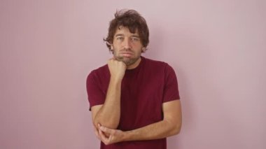 Genç İspanyol bir adam, tişört giyiyor, pembe izolasyona karşı duruyor, yorgun ve sıkılmış görünüyor. Çapraz kollar depresyon sorunlarını gösteriyor. Mutsuz düşüncelerde kaybolmuş..