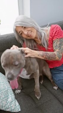 Kendinden emin orta yaşlı, kır saçlı bir kadın, köpeğiyle kanepede neşeyle oynuyor, birlikte otururken mutluluk ve sevgisini ifade ediyor.