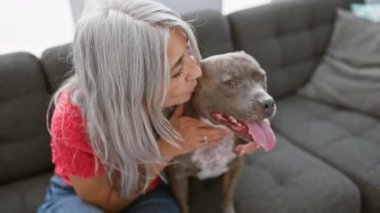 Yürek ısıtan an, gri saçlı orta yaşlı kadın köpeğiyle sevgi dolu bir öpücük paylaşıyor, birlikte kanepede oturuyor.