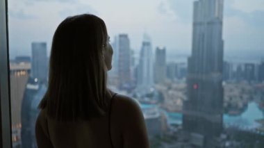 Siluetli kadın, alacakaranlıkta gözlemevinden Dubai siluetine bakıyor..