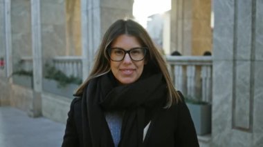 Gözlüklü gülümseyen kadın şehir merkezinde poz veriyor, zarafet ve turist havası yayıyor..