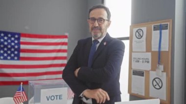 Amerikan bayrağı ve oy pusulası olan bir seçim merkezinde güvenle duran takım elbiseli olgun sakallı bir adam..