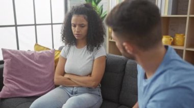 Üzgün bir kadın ve endişeli bir adam şık bir oturma odasında kanepede oturuyor, sorunlu bir ilişkiyi somutlaştırıyor..