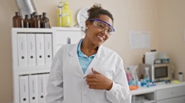 Rehabilitasyon kliniğinde güvenlik gözlüğü takmış gülümseyen Afro-Amerikan kadın bilim adamı.
