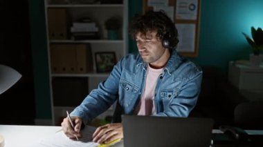 Kulaklık takan İspanyol odaklı bir adam ofis masasında geç saatlere kadar çalışıyor. Sıradan bir iş ortamında profesyonel bir yetişkinin tirajını yapıyor..