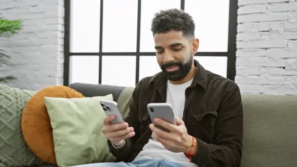 Jeune Homme Barbu Multitâche Avec Deux Smartphones Dans Salon Confortable — Video