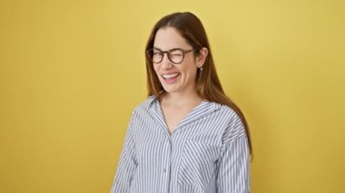 Mavi gözlü neşeli genç bir kadın, kameraya seksi bir şekilde göz kırpıyor. Gözlük takıyor, mutlu yüzü neşe saçıyor. Parlak sarı bir arka planda izole edilmiş, pozitifliğin resmidir.!