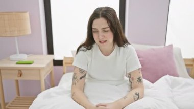 Pijamalı neşeli genç bir kadın zafer kazanmış, yataktan neşe saçan bir jest yapıyor, yatak odasına pozitiflik saçıyor.