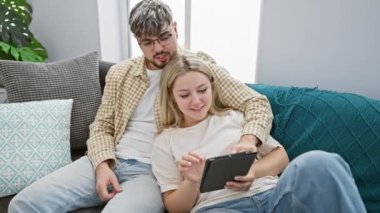 Sevgi dolu bir çift, deniz mavisi bir kanepede rahat rahat oturuyorlar, rahat bir oturma odasında dijital içeriğin tadını çıkarıyorlar..