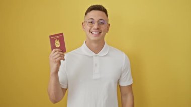 Neşeli genç İspanyol bir adam, elinde pasaport, Danimarka kimliğine güvenle bakıyor, sarı izole edilmiş bir arka planda heyecanını dile getiriyor..