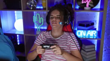 Odaklanmış kıvırcık saçlı İspanyol kadın gece renkli ve aydınlık bir oyun odasında oyun oynuyor..