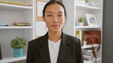 Profesyonel Asyalı takım elbiseli bir kadın modern bir ofis ortamında güvenle gülümsüyor..