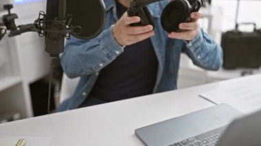 Stüdyoda mikrofon ve kulaklıklı İspanyol sakallı adam içeride müzik kaydediyor.