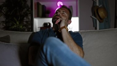 Düşünceli, orta yaşlı, gri saçlı bir adam evdeki loş ışıklı bir oturma odasında koltukta oturuyor, dalgın dalgın bakıyor.