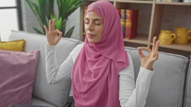 Genç, çekici İspanyol bir kadının evdeki kanepesinde dinlenirken çekilmiş huzurlu bir fotoğrafı. Şifalı yoga pozisyonu almış, tesettüre girmiş, tesettür takmış.