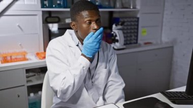 Şok olmuş Afro-Amerikalı eldivenli bilim adamı, ağızdan ağıza, şaşırmış ve korkmuş bir halde, sessiz korku ifadesi sergiliyor..