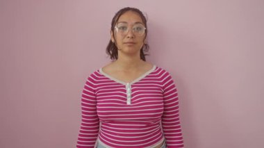 Çizgili tişörtlü neşeli İspanyol kadın pozitif titreşimler yayıyor, kendine güvenen dişlek bir gülümseme, pembe arka planda tek başına duruyor.