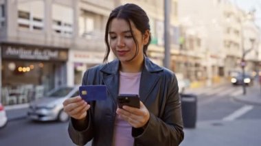 Kentsel caddede elinde kredi kartı ve akıllı telefon tutan İspanyol kadın.