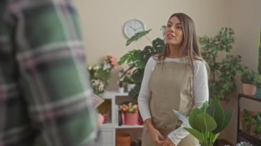 Önlüklü gülümseyen bir kadın, kapalı bir çiçekçide erkek bir müşteriden ödeme kabul ediyor..