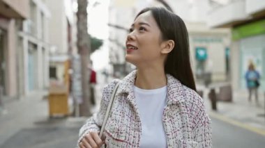 Genç bir Asyalı kadın, şehir caddesinde yürürken gülümsüyor, kendine güveni ve tarzı ile.