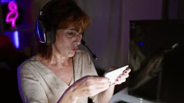Gece karanlık bir oyun odasında akıllı telefon kullanan odaklanmış bir kadın..