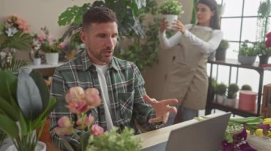 Videodaki adam çiçekçi kadınla çiçekçide bitki ve dekorasyonları tartışıyor..