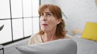 Orta yaşlı bir kadın öfke nöbeti geçiriyor, yatakta oturuyor, yastığa sarılıyor, yatak odasında çığlık atıyor, saf öfke saçıyor.