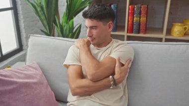 Kanepede oturan yakışıklı, genç İspanyol bir adam. Evinin rahat ortamında kendine sarılıyor. Işıldayan pozitiflik, o kendini sevme ve neşe resmidir, mutlu bir şekilde kendine güvenir..