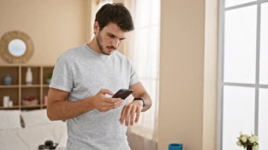 Sakallı, akıllı telefon kullanan ve parlak, rahat bir yatak odasında akıllı bir genç adam..