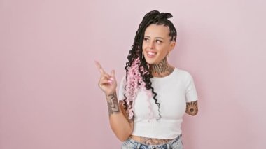 Göz alıcı İspanyol ampüte kadın kendinden emin duruyor, yüzünde güven dolu bir gülümseme ile yan tarafa bakıyor, pembe bir arka plan üzerinden kameraya bakıyor.