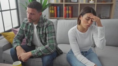 Düşünceli bir erkek ve kadın, gri bir kanepede ayrı otururlar. İç mekan içinde gerginlik yaratırlar..