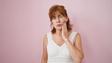 Orta yaşlı kadın ayakta duruyor, dişleri ağrıdığı için dudaklarına dokunuyor. diş ağrısı ifadesi pembe arkaplanda izole edildi
