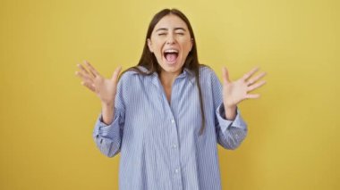 Muzaffer genç İspanyol kadın çılgın zaferi çılgınca kutluyor! Güzel, sarı arka planda duruyor, kollar çılgın bir zafer jesti içinde, kazanan tişörtü giyiyor, başarı için heyecanlı..