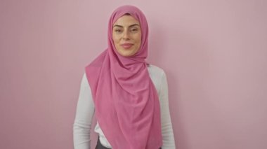 Neşeli, tesettürlü genç İspanyol kadın başparmaklarını kaldırarak sevinçle yüzünü işaret ediyor, iyimser bir gülümseme sergiliyor, izole edilmiş pembe bir arka planda ağzı açık.!