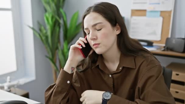 一个年轻的高加索女人在办公室里做着多项任务 一边用智能手机说话 一边检查她的聪明 — 图库视频影像
