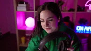 Kafkasyalı genç bir kadın, mor ışıklarla aydınlatılmış karanlık bir odada, mikrofonlu bir kulaklık takarak oyun oynamaktan hoşlanıyor..