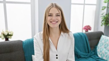 Sarışın kadın elinde evin anahtarını tutarak gülümsüyor. Parlak bir oturma odasında ev sahipliğini simgeliyor..