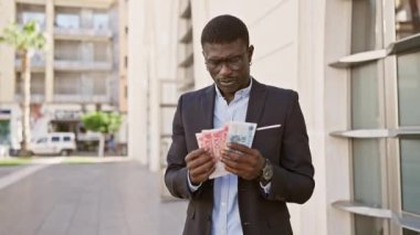 Takım elbiseli gülümseyen Afrikalı bir adam Çin Yuan banknotlarını şehir sokaklarında karşılaştırıyor.