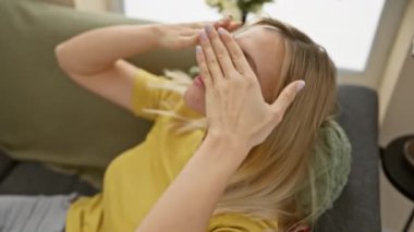 Genç sarışın kadın tişört giyiyor. Gözleri kapıyor. Gülümsüyor ve gülümsüyor. Kör kavram. evde.